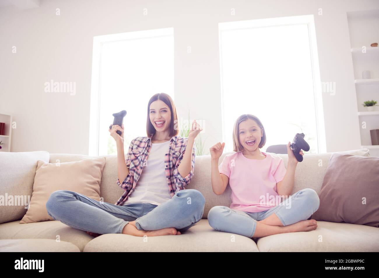 Portrait of two attractive cheerful girls sitting on divan playing video game having fun at home flat indoors Stock Photo