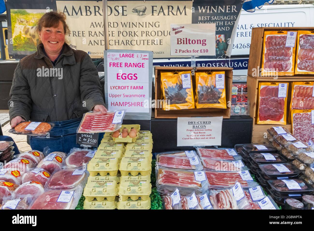 England, Hampshire, Petersfield, Weekly Farmers Market, Smiling Lady Selling Meat Products Stock Photo