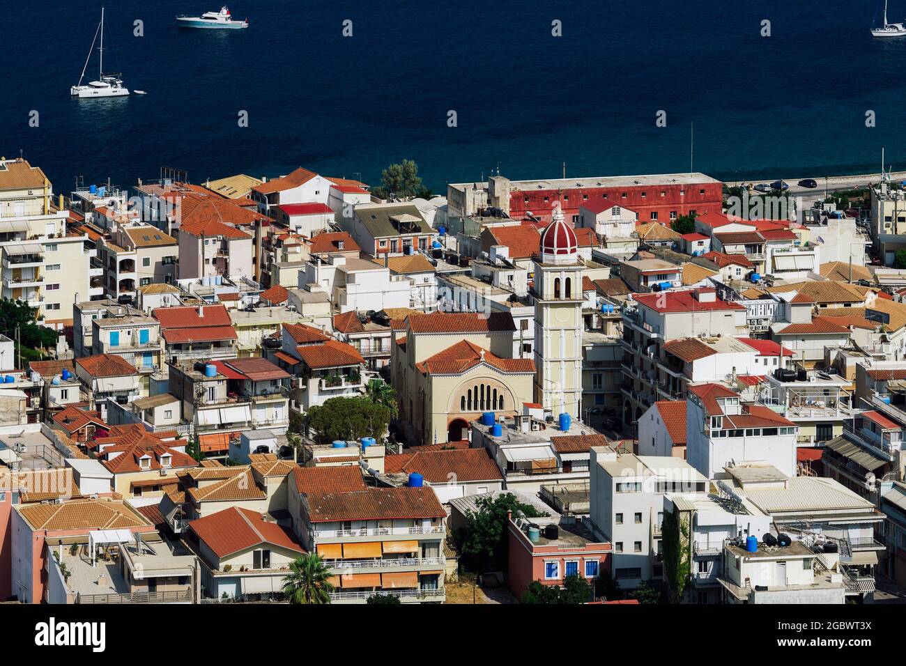 Zakynthos, Greece Island capital panorama with low rise buildings. Sunny view of Orthodox church around red tile houses, next to calm see waterfront. Stock Photo