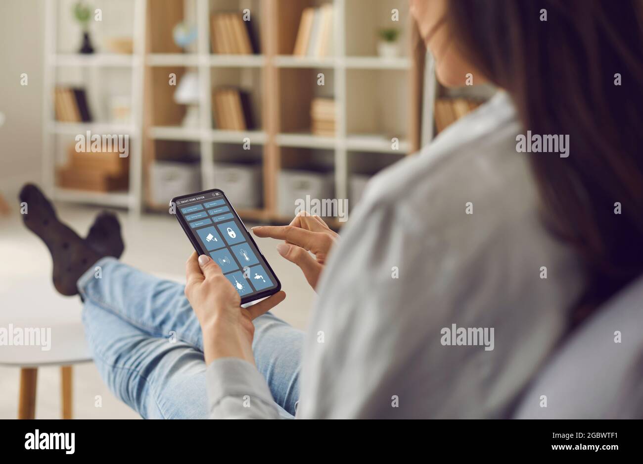 Woman controls the system of her modern Smart House using an app on her smartphone Stock Photo