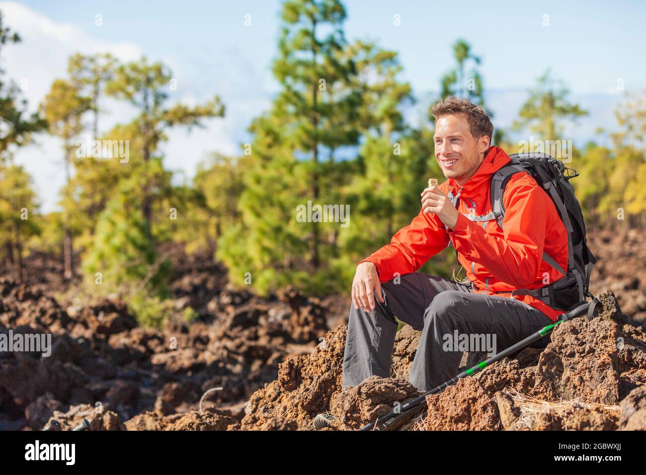 Hiking man eating granola protein bar snack during mountain hike travel