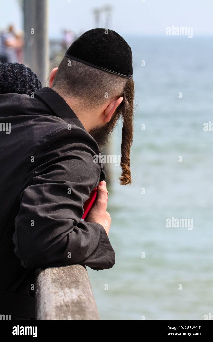 Back Of A Young Male Hasidic Jew With Long Payot Sideburns Wearing a Rekel Looking Out To Sea England UK Stock Photo