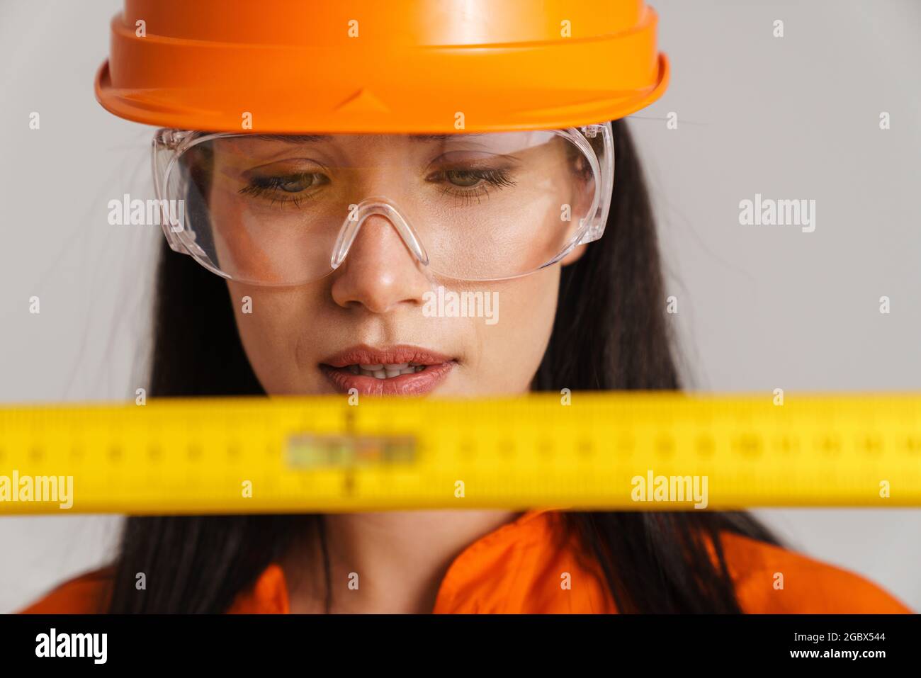 Young woman in safety glasses and helmet posing with tape measure