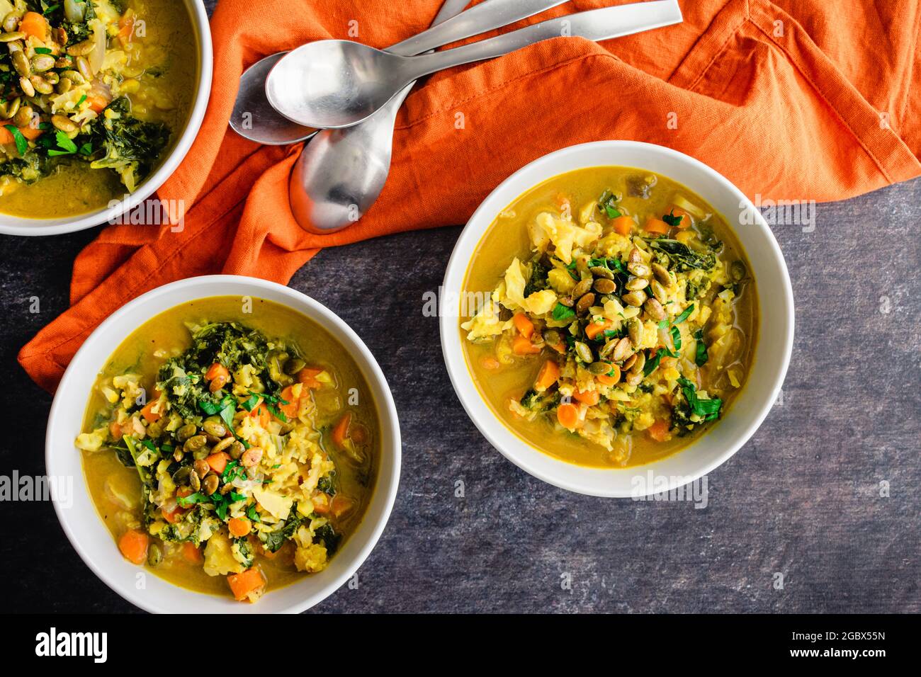 Bowls of Vegan Curried Cauliflower Rice Kale Soup: Curried vegetable soup garnished with toasted pumpkin seeds and parsley Stock Photo