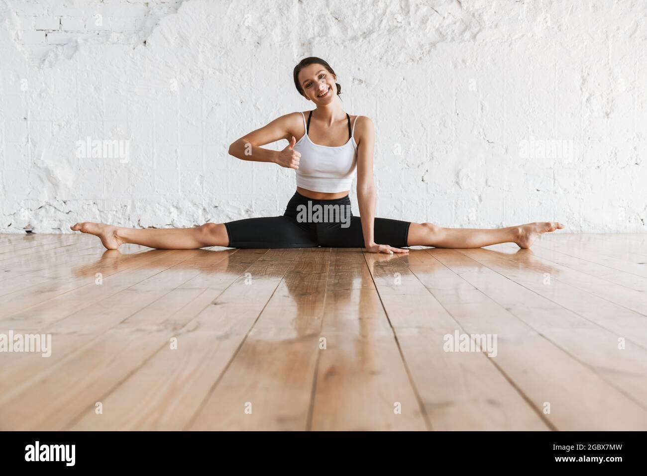 Smiling young brunette white woman on sportswear sitting in split on a ...