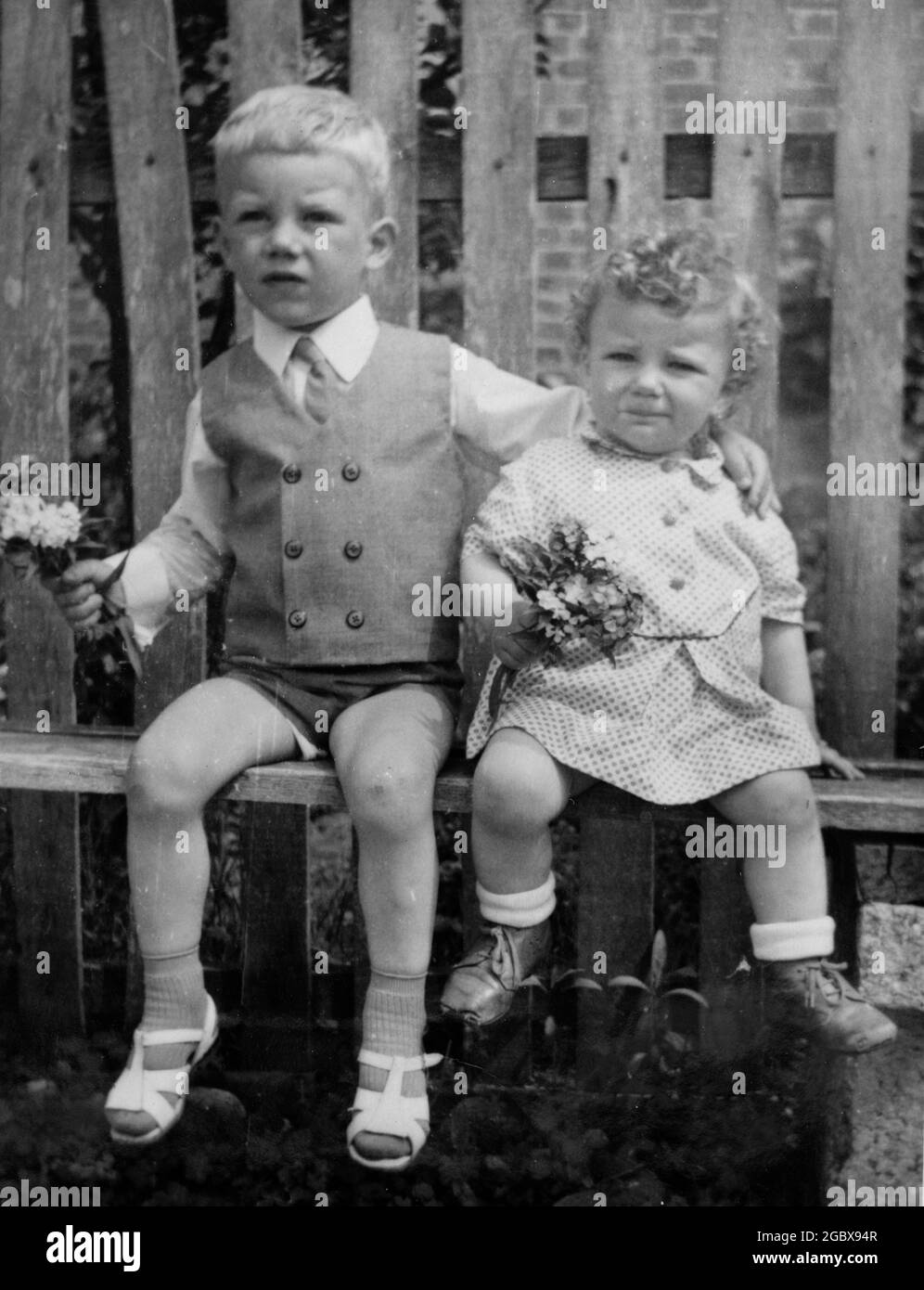Two siblings sitting on simple wooden bench hugging and smiling. Archival photo circa 1969. Bulgaria, Balkans, Europe Stock Photo