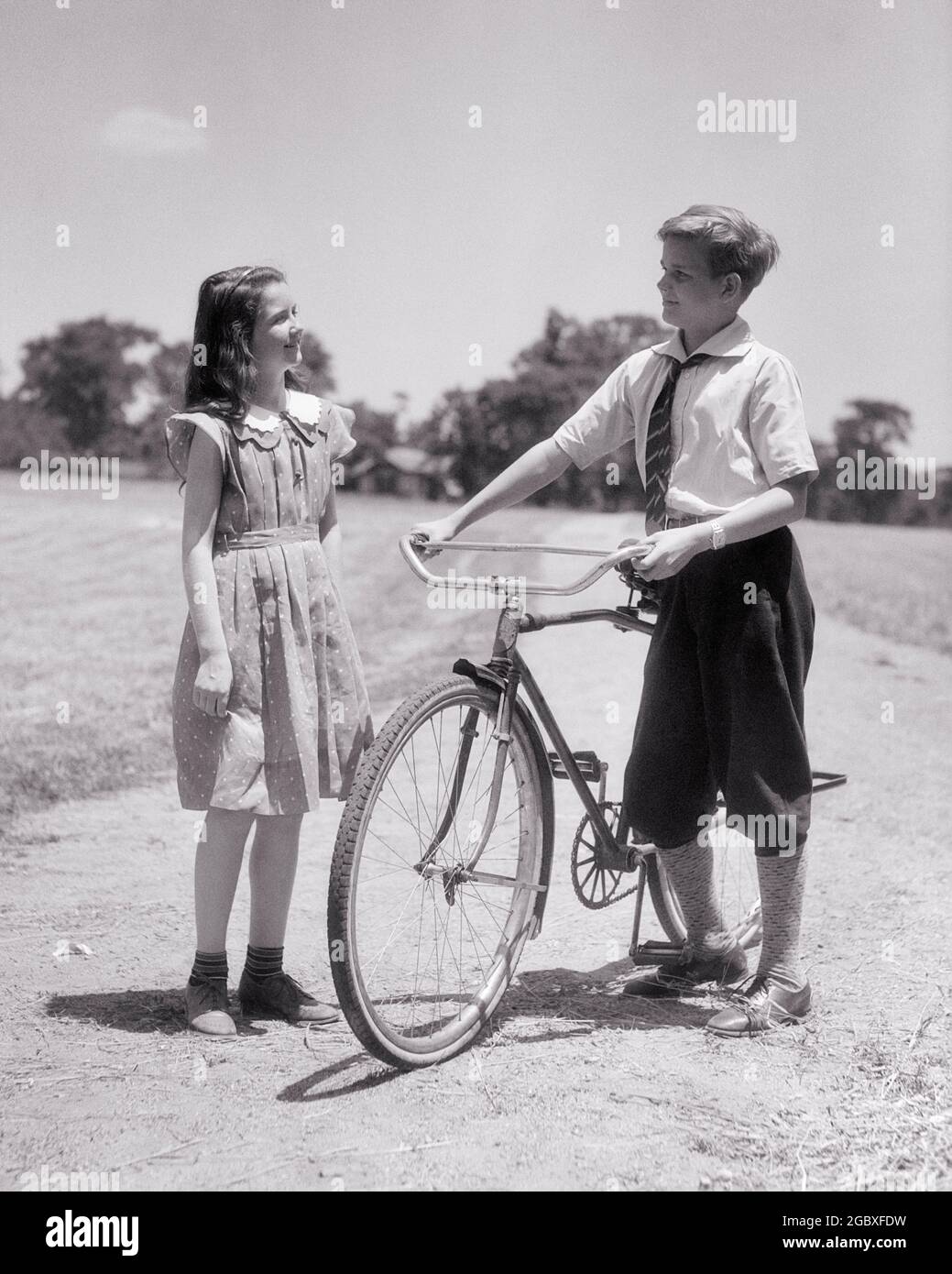 1940s SMILING PRE-TEEN GIRL SISTER TALKING WITH OLDER BROTHER WEARING KNICKERBOCKERS STANDING HOLDING BICYCLE ON PARK PATH - b14498 HAR001 HARS 1 FITNESS JUVENILE STYLE COMMUNICATION HEALTHY BALANCE PANTS KNICKERS JOY LIFESTYLE FEMALES BROTHERS BIKING HEALTHINESS COPY SPACE FRIENDSHIP FULL-LENGTH PERSONS CARING MALES SIBLINGS CONFIDENCE BICYCLES SISTERS TRANSPORTATION B&W BIKES ACTIVITY PATH HAPPINESS PHYSICAL WELLNESS STRENGTH TROUSERS EXCITEMENT RECREATION PRIDE ON OPPORTUNITY SIBLING TRAIL CONNECTION CONCEPTUAL FLEXIBILITY MUSCLES STYLISH KNICKERBOCKERS PLUS FOURS GROWTH PRE-TEEN Stock Photo
