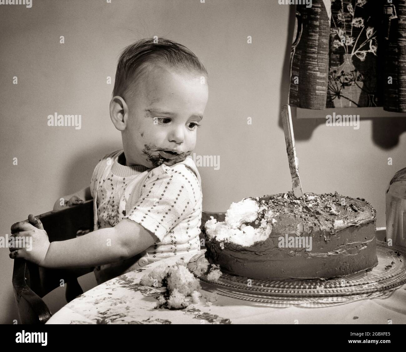 1950s GUILTY LITTLE BOY LOOKING AT PARTIALLY EATEN WHOLE LAYER CAKE CHOCOLATE ICING ALL OVER HANDS AND FACE  - b2082 JHN001 HARS CAKES HOME LIFE COPY SPACE HALF-LENGTH MALES ALL ICING B&W HUMOROUS HIGH ANGLE MISCHIEF AND EXCITEMENT LAYER COMICAL FROSTING AT COMEDY WHOLE BABY BOY EATEN GROWTH GUILTY JUVENILES MISBEHAVING PARTIALLY BLACK AND WHITE CAUCASIAN ETHNICITY MISBEHAVIOR OLD FASHIONED Stock Photo