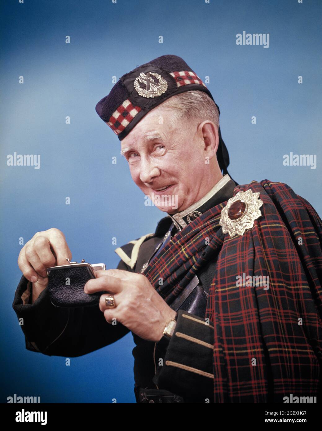 1950s 1960s SMILING CHARACTER MAN IN SCOTTISH TARTAN MILITARY COSTUME PUTTING A COIN INTO A CHANGE PURSE PINCHING A PENNY - kc1212 HAR001 HARS OLDSTER BROOCH FRUGAL SMILES TARTAN ELDERS GLENGARRY SCOT JOYFUL SCOTCH ECONOMICAL ELDERLY MAN PENNY-PINCHING SMART PARSIMONIOUS REGIMENTAL BADGE CAUCASIAN ETHNICITY DICING HAR001 OLD FASHIONED Stock Photo