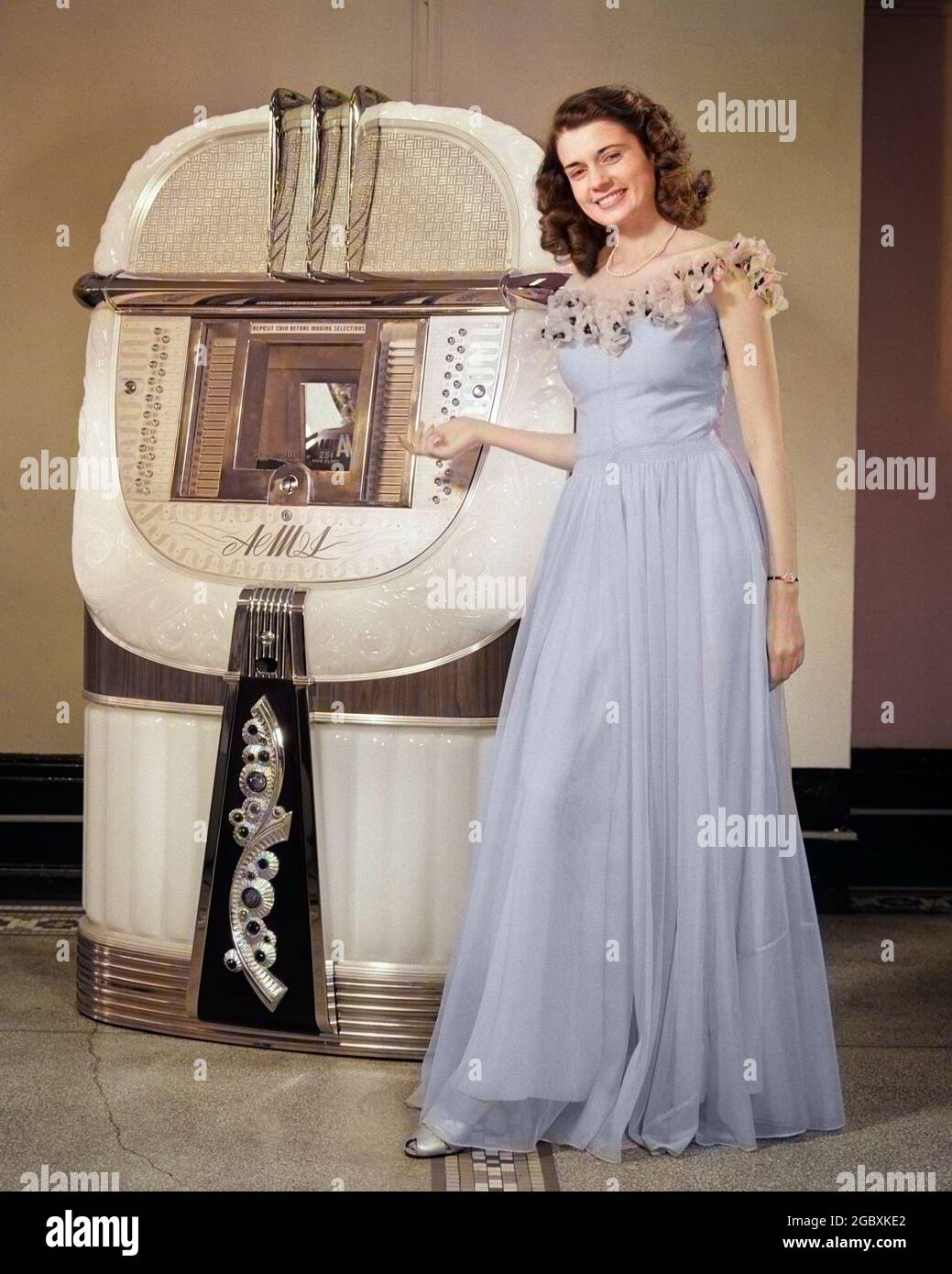 1940s PORTRAIT OF YOUNG SMILING BRUNETTE WOMAN IN LILAC BALL GOWN LOOKING  AT CAMERA STANDING IN FRONT OF AND POINTING AT JUKEBOX - o3883c HAR001 HARS  PROM PLAYER CLOTHING INDOORS FLOOR RECORD