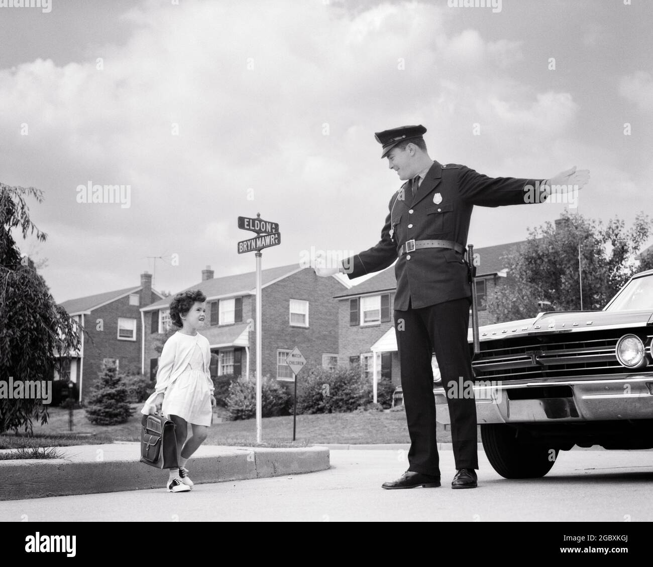 1960s SMILING POLICE OFFICER MAN STOPPING CAR TRAFFIC TO LET LITTLE SCHOOL GIRL CARRYING BOOK BAG SAFELY CROSS SUBURBAN STREET  - p6950 HAR001 HARS AUTO 1 POLICEMAN JUVENILE COMMUNICATION SERVE VEHICLE SAFETY PUBLIC PLEASED JOY LIFESTYLE FEMALES COPY SPACE FULL-LENGTH PERSONS AUTOMOBILE CARING MALES RISK ORDER OFFICER CONFIDENCE TRANSPORTATION B&W COP WIDE ANGLE PROTECT CHEERFUL ADVENTURE PROTECTION STRENGTH AND AUTOS POWERFUL PRIDE TO AUTHORITY OCCUPATIONS SMILES UNIFORMS CONCEPTUAL AUTOMOBILES JOYFUL STOPPING VEHICLES LET OFFICERS POLICEMEN COPS GROWTH JUVENILES MID-ADULT MID-ADULT MAN BADGE Stock Photo