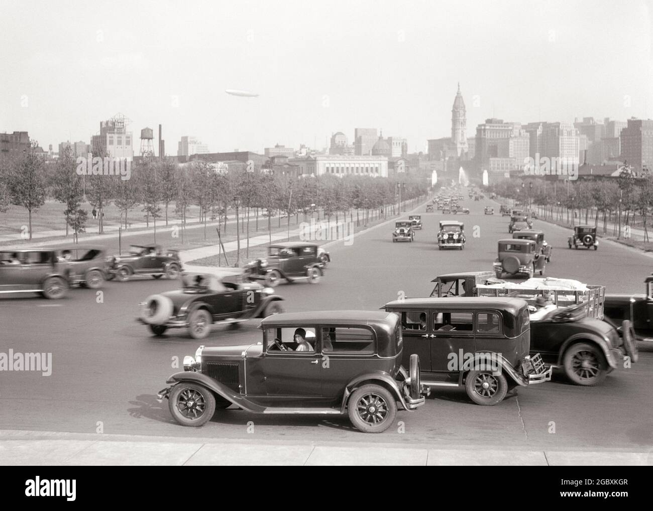 1920s 1930s CARS TRAFFIC ON BENJAMIN FRANKLIN PARKWAY LOOKING SOUTHEAST TO CITY HALL AND DOWNTOWN SKYLINE PHILADELPHIA PA USA - p2880 HAR001 HARS SOUTHEAST DIRECTION PRIDE BEN FRANKLIN ON TO CONCEPTUAL AUTOMOBILES BENJAMIN FRANKLIN PARKWAY STYLISH VEHICLES TREE LINED GROWTH PARKWAY BENJAMIN FRANKLIN BLACK AND WHITE HAR001 OLD FASHIONED Stock Photo
