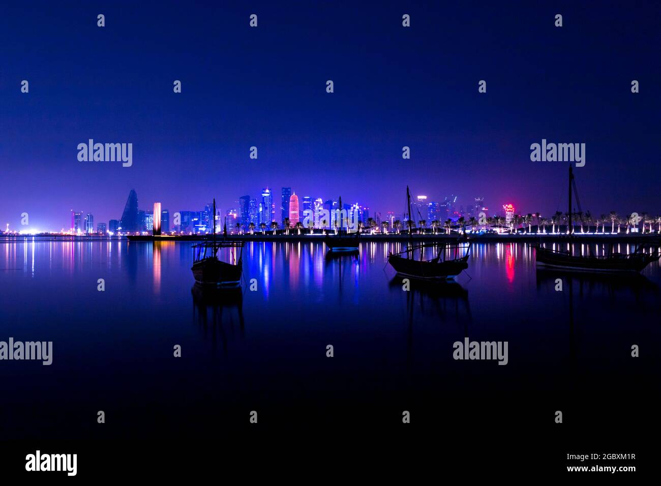Coloful illuminated skyline of Doha at night with traditional wooden boats called Dhows in the foreground, Qatar, Middle East against dark sky Stock Photo