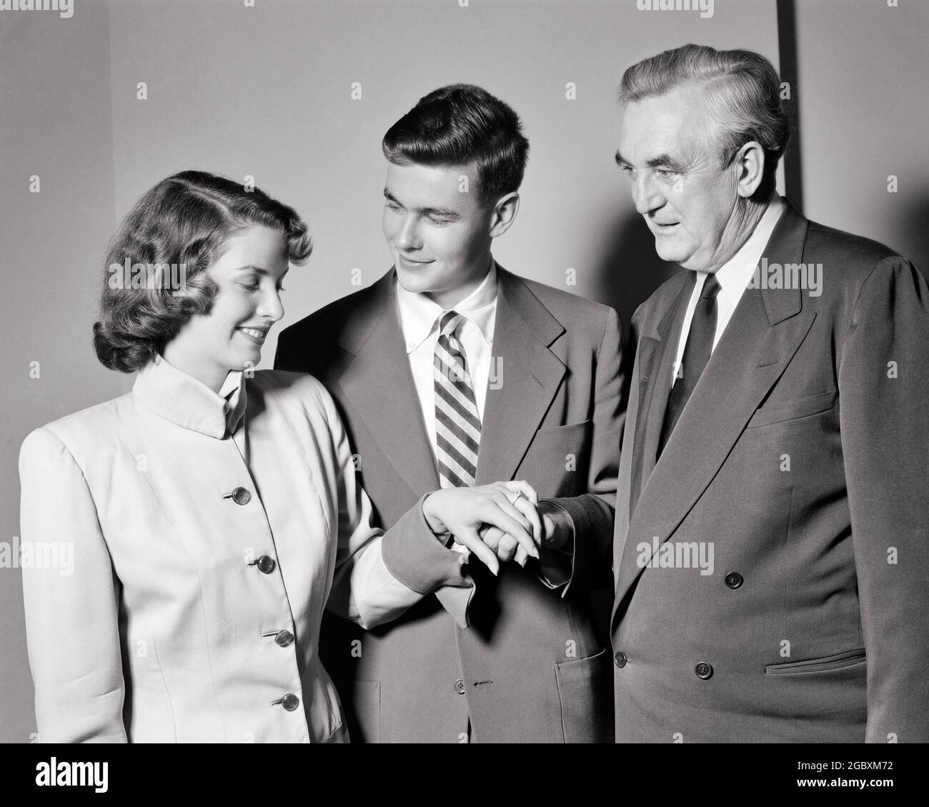 1950s JUST BETROTHED YOUNG MAN AND WOMAN COUPLE SHOWING ENGAGEMENT DIAMOND  RING TO ADMIRING FATHER - s5526 HAR001 HARS FUTURE NOSTALGIA OLD FASHION 1  STYLE WELCOME YOUNG ADULT TEAMWORK STRONG JOY LIFESTYLE