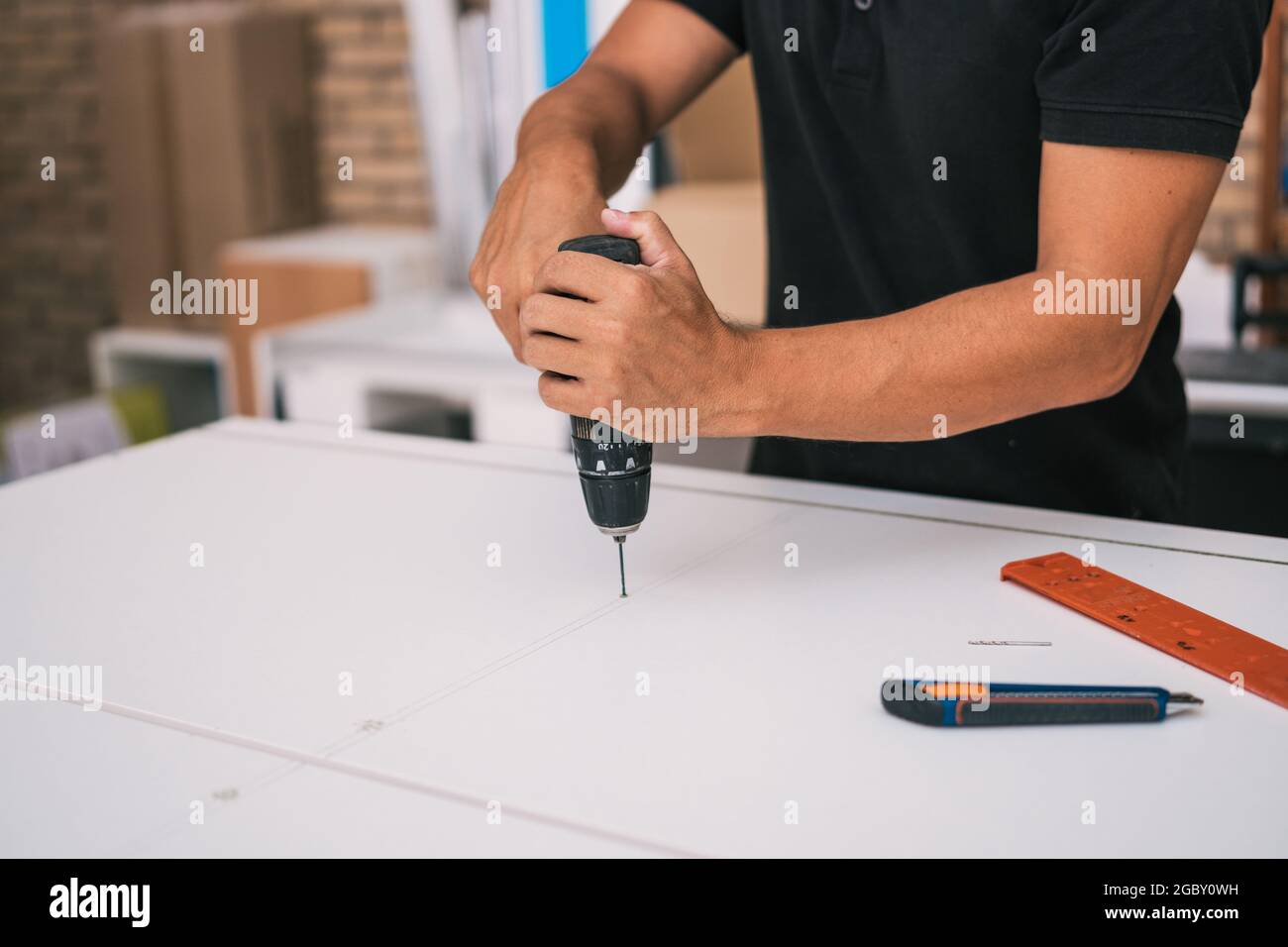 Man using a drill to make a small hole in a white surface in a