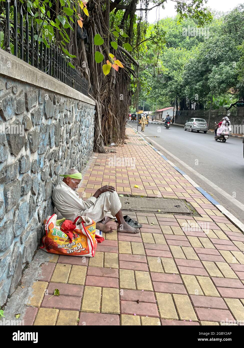 A poor and homeless man siting on the pavement besides a road with ...