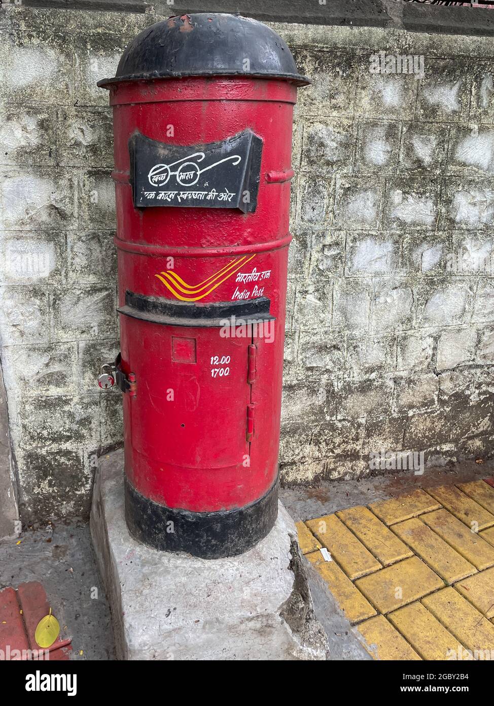 A vintage red colored post box also called letter box standing vertical besides a wall at Pune India on 7 July 2021 Stock Photo