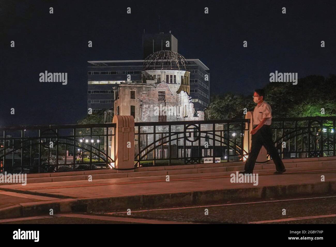Hiroshima, Japan. 05th Aug, 2021. A man wearing a face mask as a precaution against the spread of covid-19 walks past the Atomic Bomb Dome that lights up at night. This Friday will mark the 76th anniversary of the atomic bombing of Hiroshima, which killed about 150,000 people and destroyed the entire city for the first bombing with a nuclear weapon in war. Limited guests and Japan's dignitaries including Prime Minister Yoshihide Suga will attend the Peace Memorial Ceremony amid the coronavirus pandemic. Credit: SOPA Images Limited/Alamy Live News Stock Photo