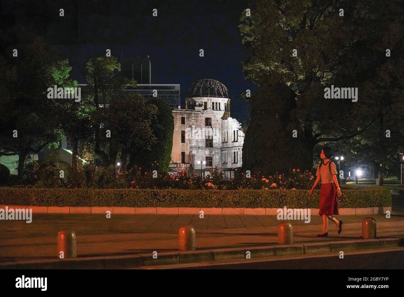 Hiroshima, Japan. 05th Aug, 2021. A woman wearing a face mask as a precaution against the spread of covid-19 walks past the Atomic Bomb Dome that lights up at night.This Friday will mark the 76th anniversary of the atomic bombing of Hiroshima, which killed about 150,000 people and destroyed the entire city for the first bombing with a nuclear weapon in war. Limited guests and Japan's dignitaries including Prime Minister Yoshihide Suga will attend the Peace Memorial Ceremony amid the coronavirus pandemic. Credit: SOPA Images Limited/Alamy Live News Stock Photo