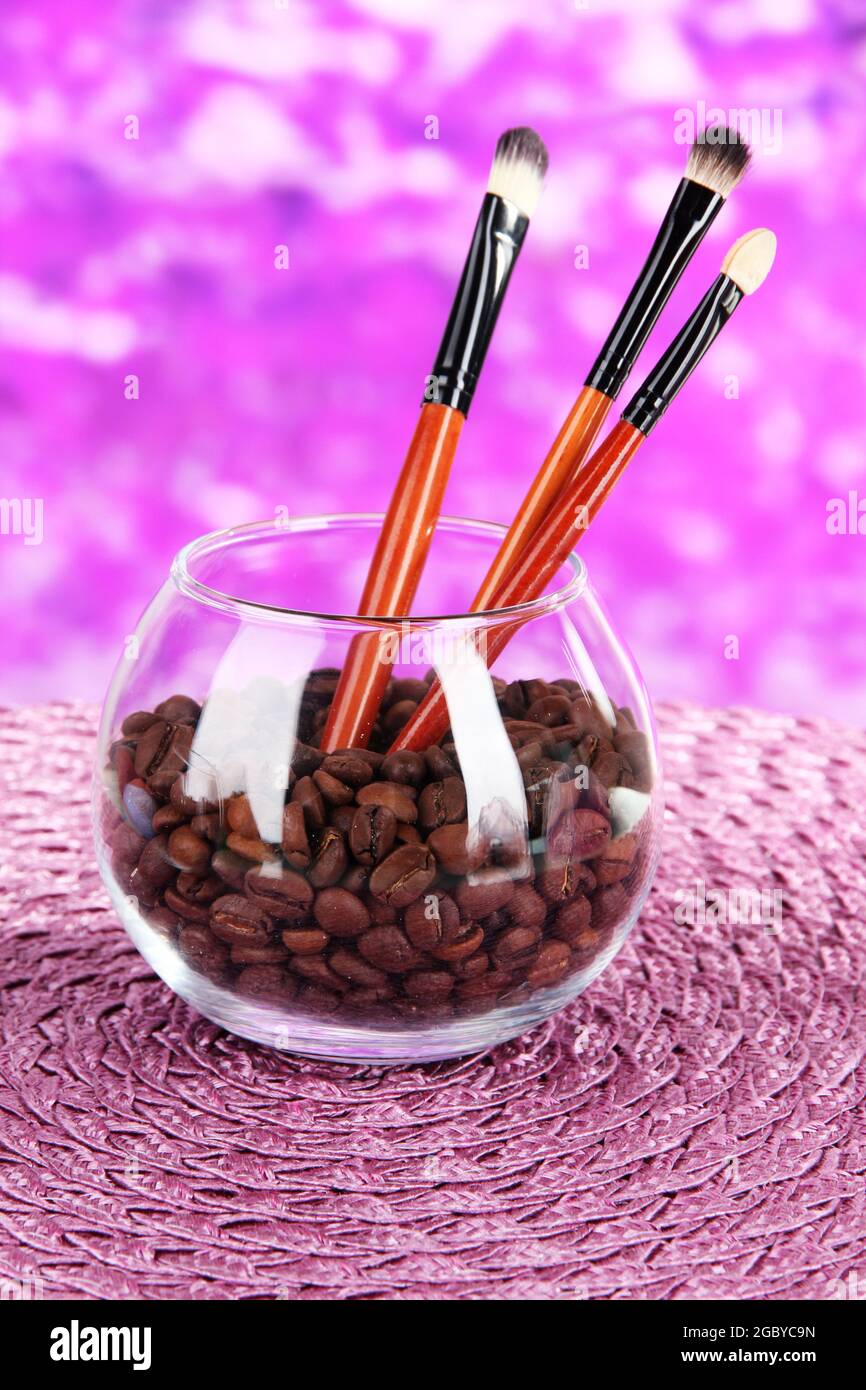 Glass bowl with coffee beans and brushes on bright background Stock