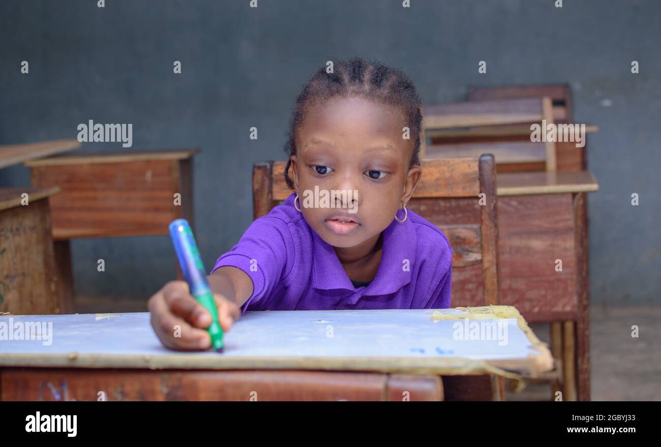 African girl child, pupil or student sitting down and writing in a classroom while studying for excellence in her school, education and career Stock Photo