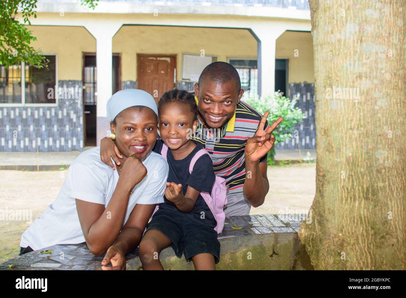 African mother and father or guardian sitting together with their daughter in a school environment, available to help the girl child attain excellence Stock Photo