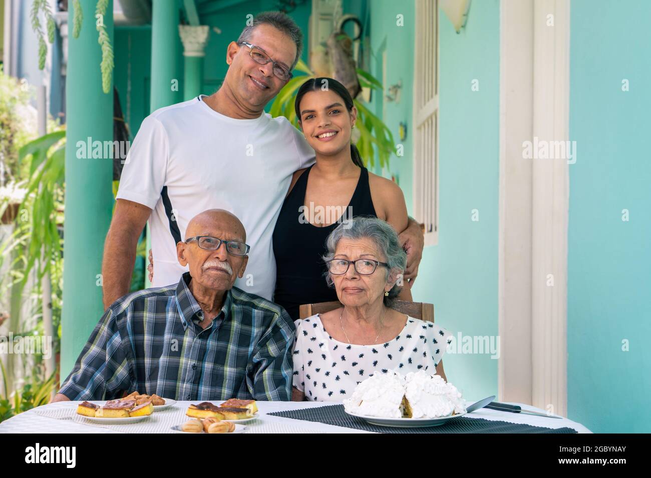 Elderly couple wearing eyeglasses sitting at a table and a man and a young woman standing behind the elderly Stock Photo