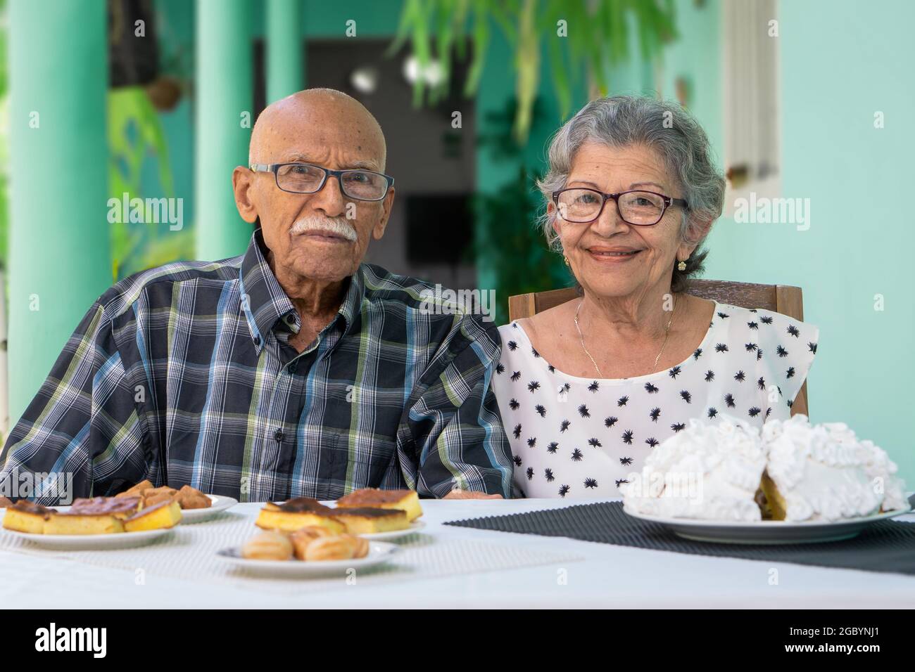 Elderly couple wearing eyeglasses sitting at a table looking at the camera Stock Photo
