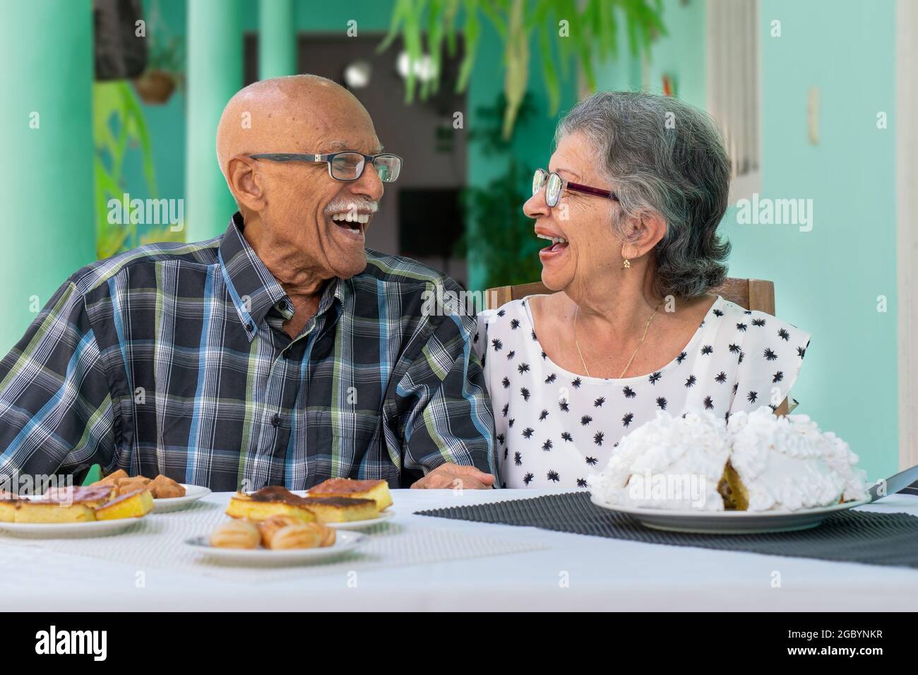 Elderly couple wearing glasses sitting at a table, both are smiling Stock Photo