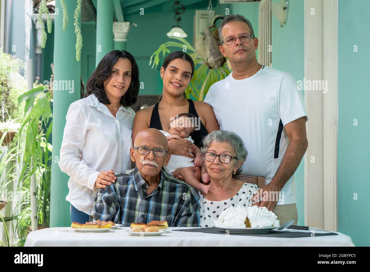 Elderly couple sitting. A man a woman and a young woman with a child in their arms standing behind the elderly couple Stock Photo