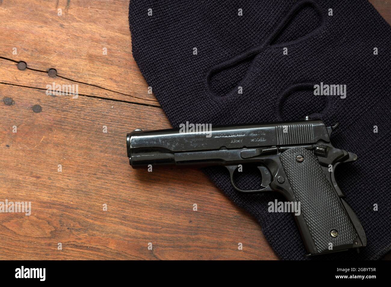 Pistol gun and a balaclava on wooden background. Black metal weapon and