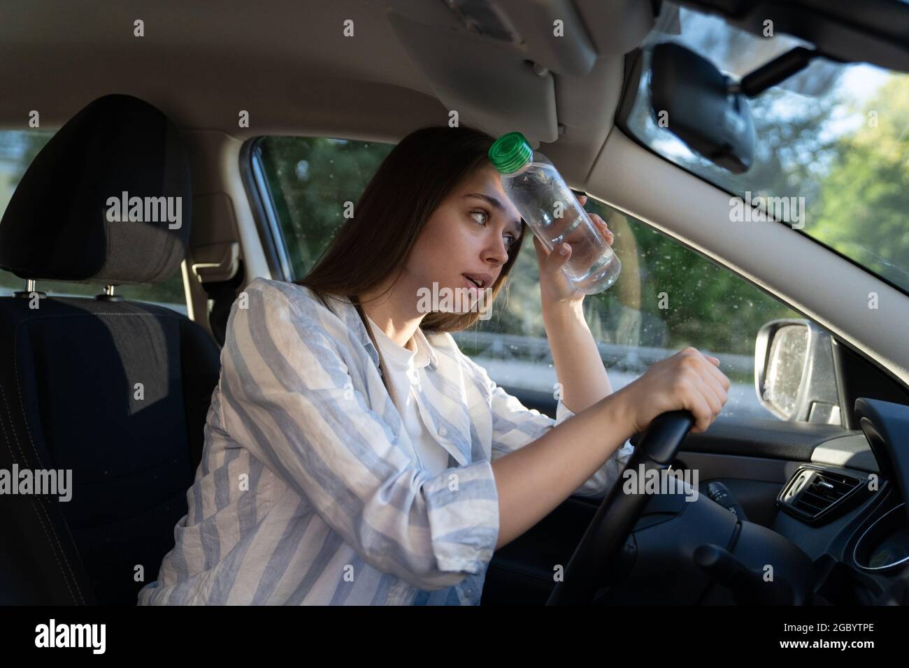 Exhausted girl driver suffering from headache, heat, hot weather applies bottle of water to forehead Stock Photo