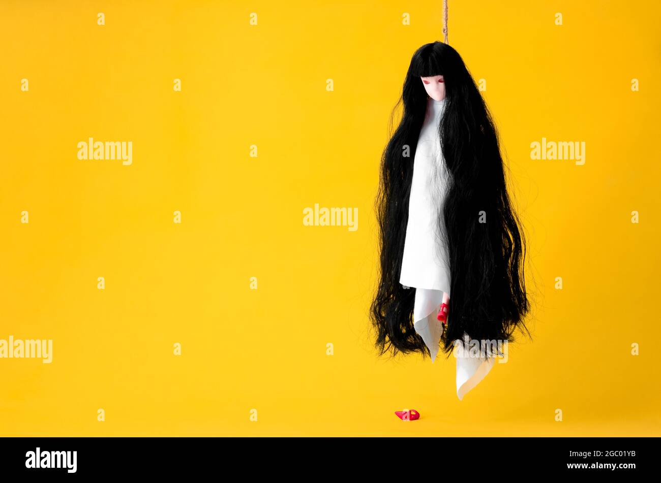 Long hair asian female ghost hanging with the rope acting commit suicide on orange background. Minimal Halloween scary concept. Stock Photo