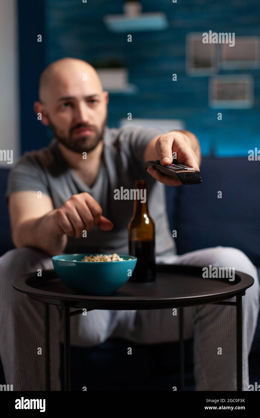 Scared shocked man looking at horror thriller movie at tv, eating popcorn trembled with fright sitting on comfortable sofa. Concentrated alone male watching tv late night enjoying free time Stock Photo