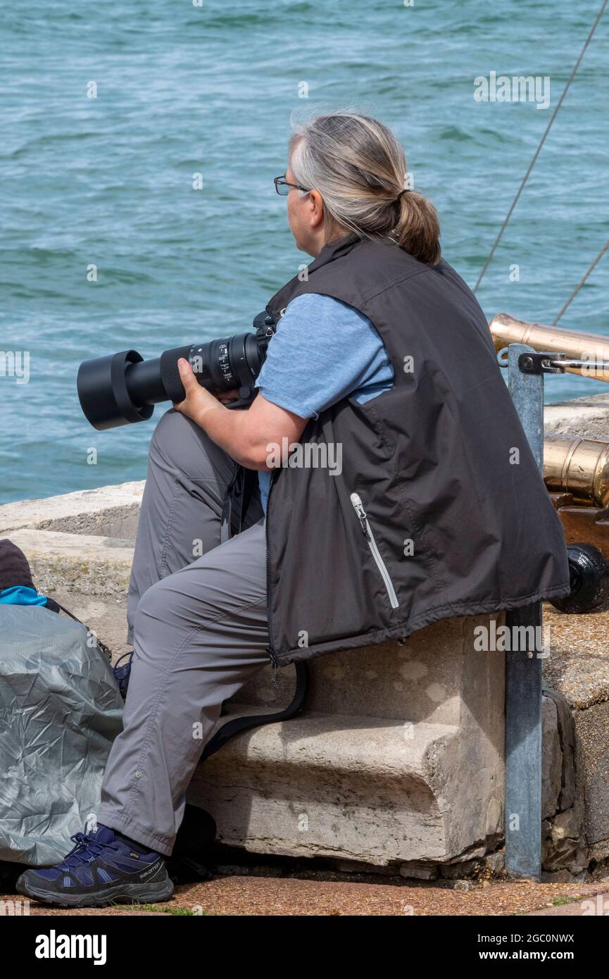 Female photographer taking pictures at Cowes week, lady taking photographs at sailing regatta, lady using camera with long telephoto lens. Stock Photo