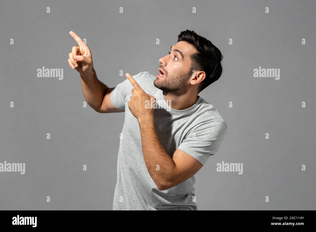 Shocked young Caucasian man gasping with hands pointing up isolated light gray studio background Stock Photo