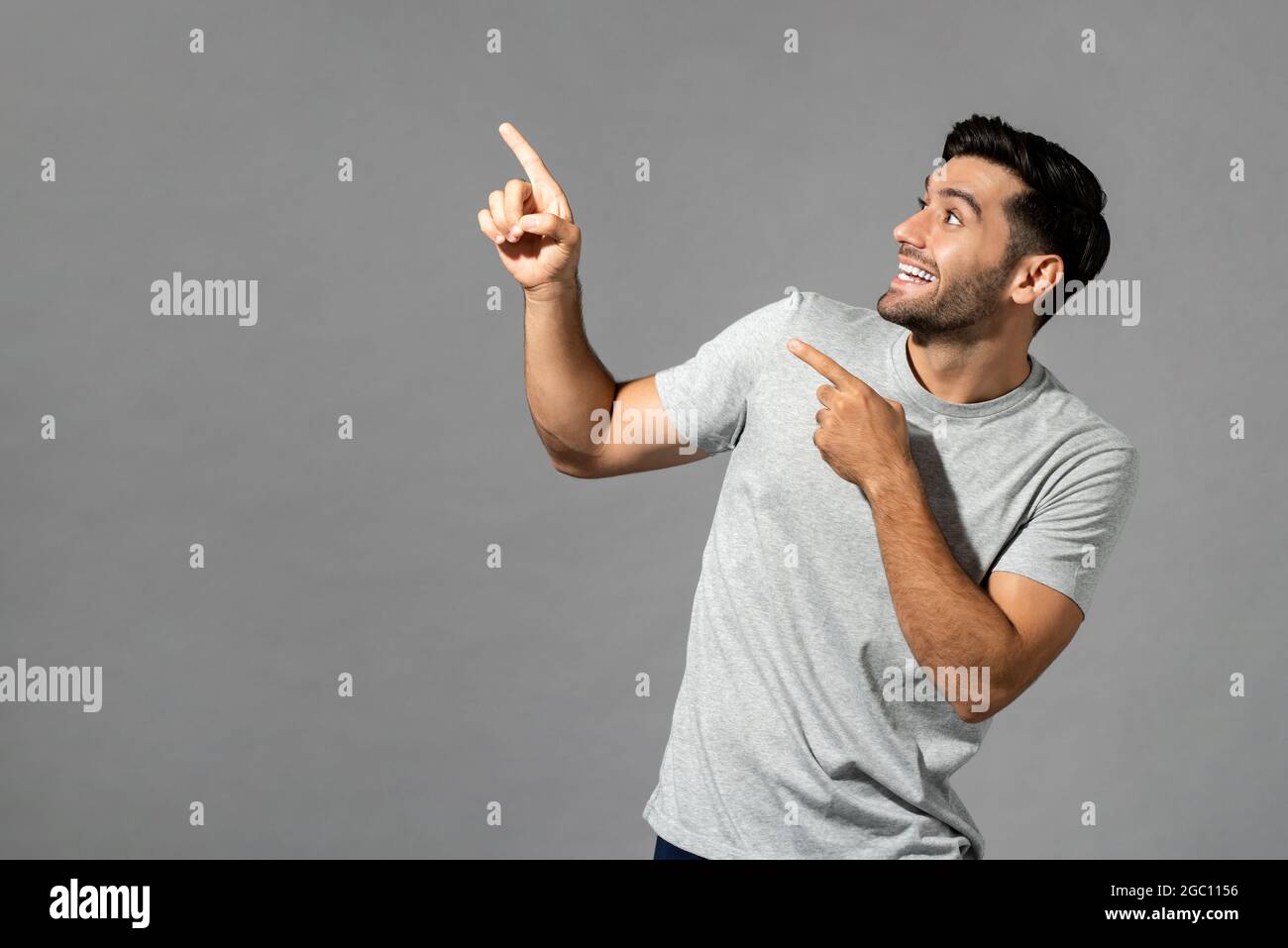 Portrait of surprised young Caucasian man with hands pointing up in isolated light gray studio background Stock Photo
