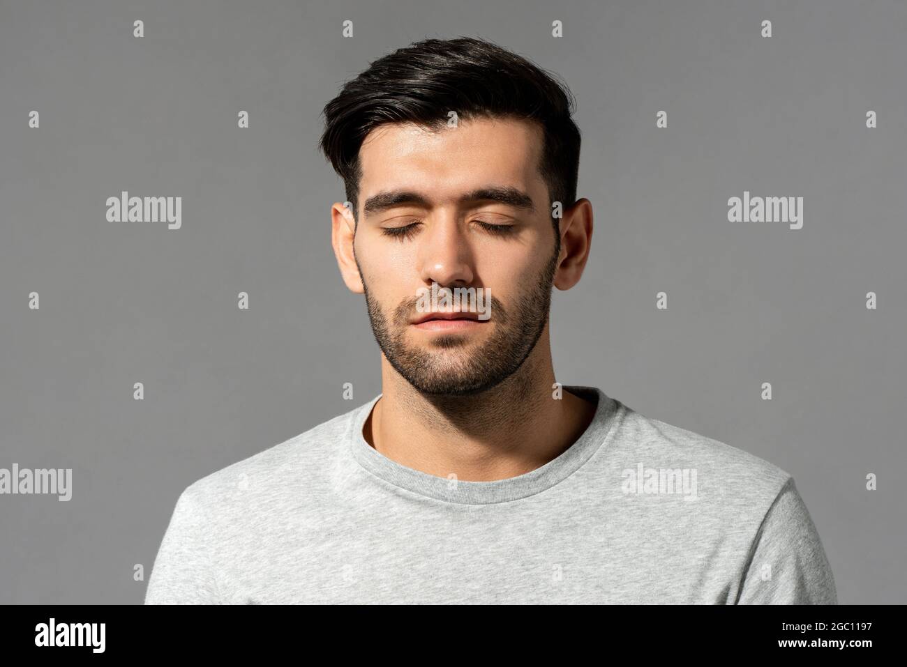 Close up portrait of serene young Caucasian man face with eyes closing on isolated light gray studio background Stock Photo
