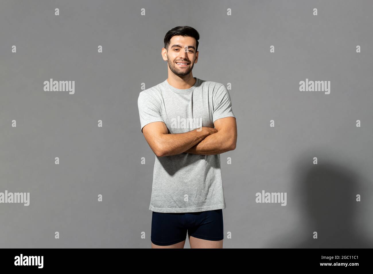 Happy cheerful young Caucasian millennial man in sleepwear standing with arms crossed on isolated light gray studio background Stock Photo