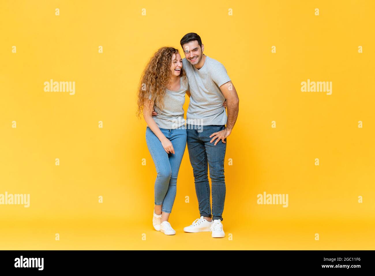 Full length portrait of young happy interracial millennial couple holding each other and laughing in isolated yellow studio background Stock Photo