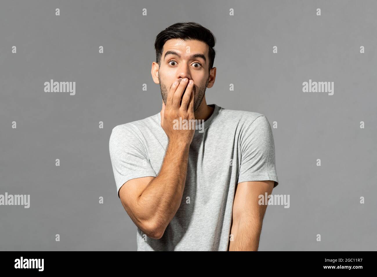 Portrait of shocked young Caucasian man with hand covering mouth on light gray studio background Stock Photo
