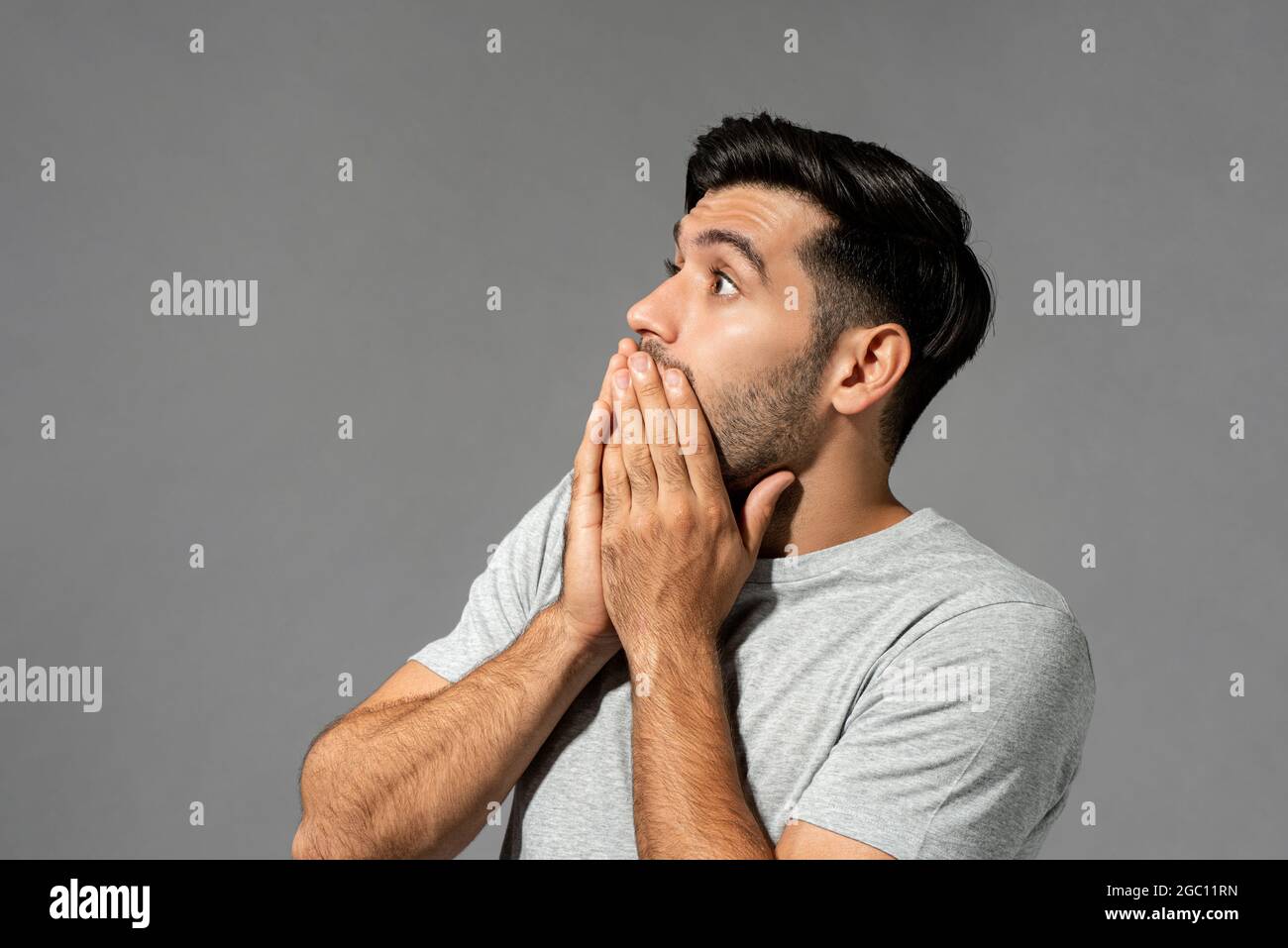 Shocked scared young Caucasian man with eyes popping and hands covering mouth on light gray studio background Stock Photo