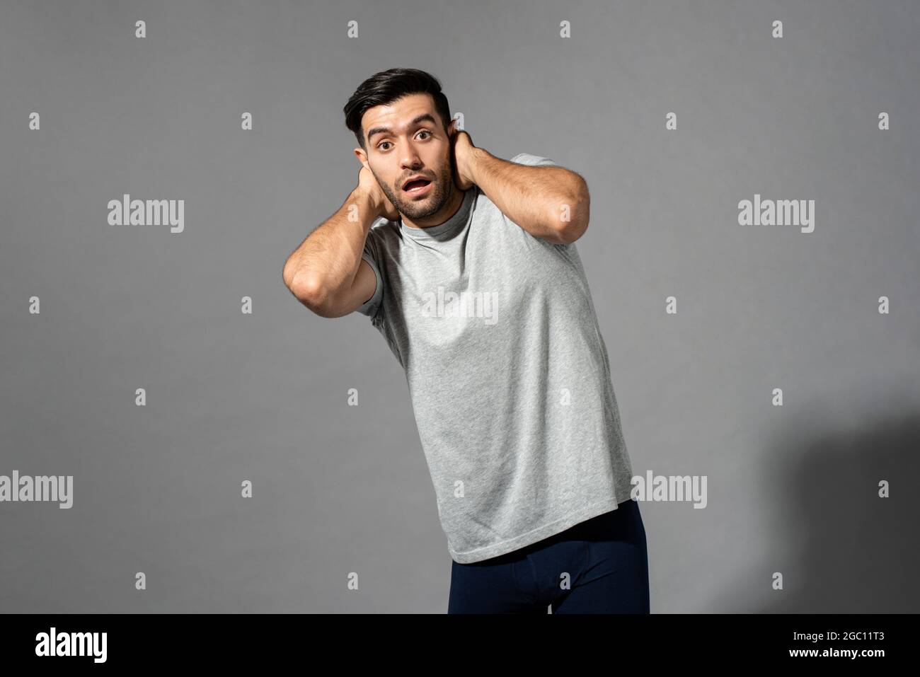 Surprised young Caucasian man gasping with hands behind neck on light gray isolated studio background Stock Photo
