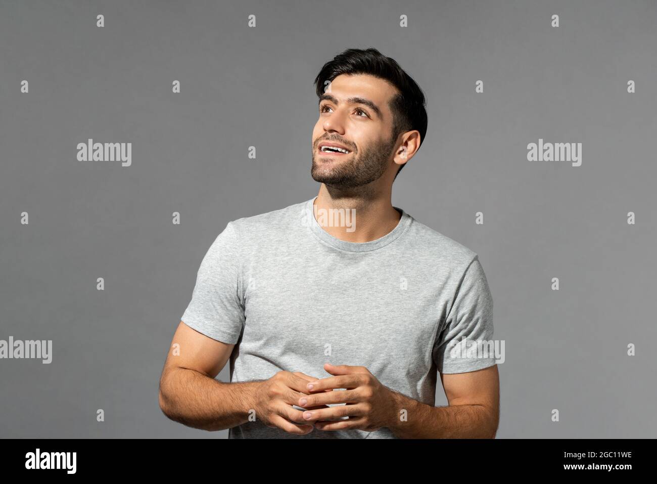 Thinking handsome young Caucasian man with hands looking upward on light gray studio background Stock Photo