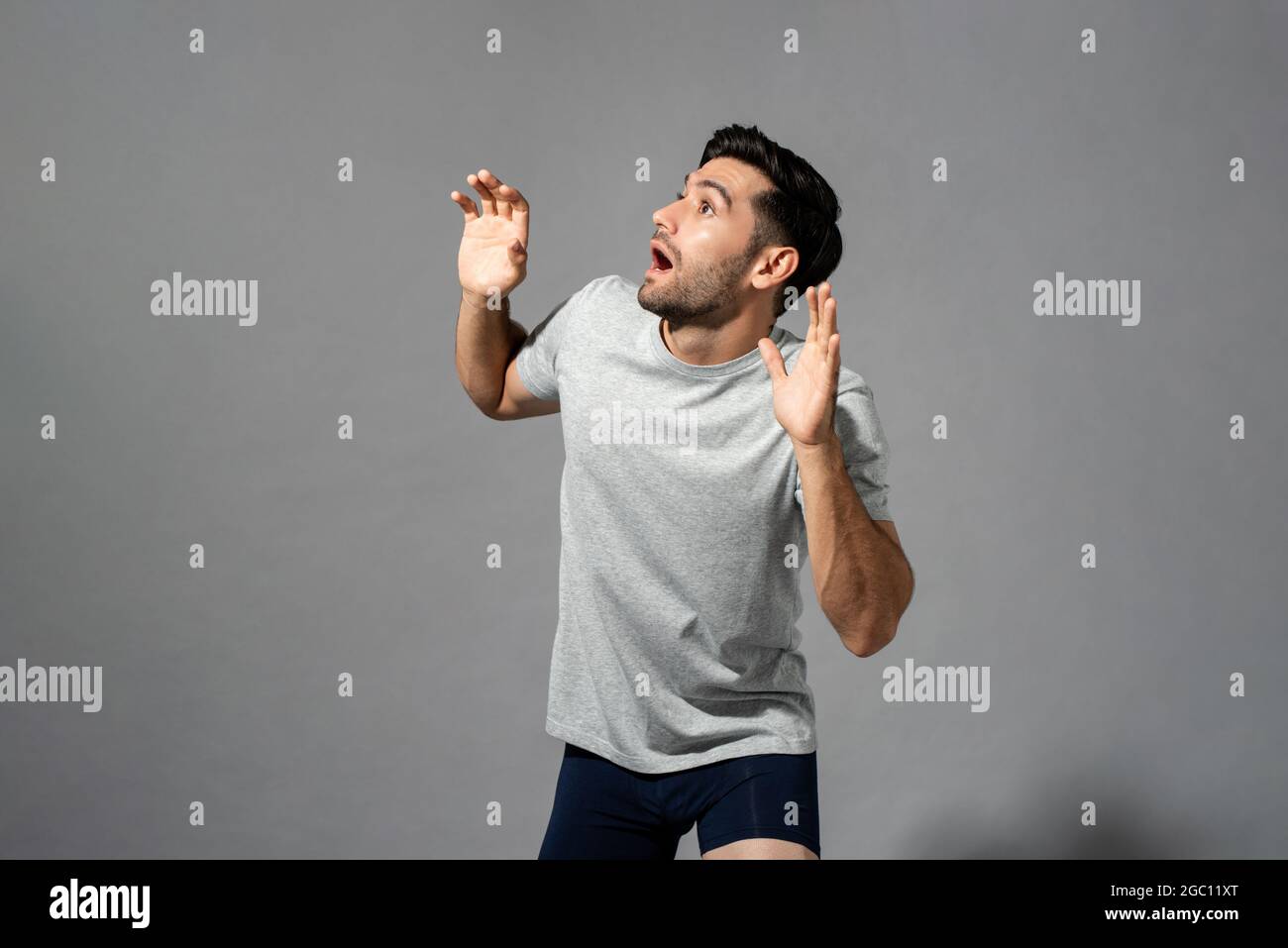 Surprised shocked young Caucasian man with open hands gesture looking aside and gsaping in light gray isolated studio background Stock Photo