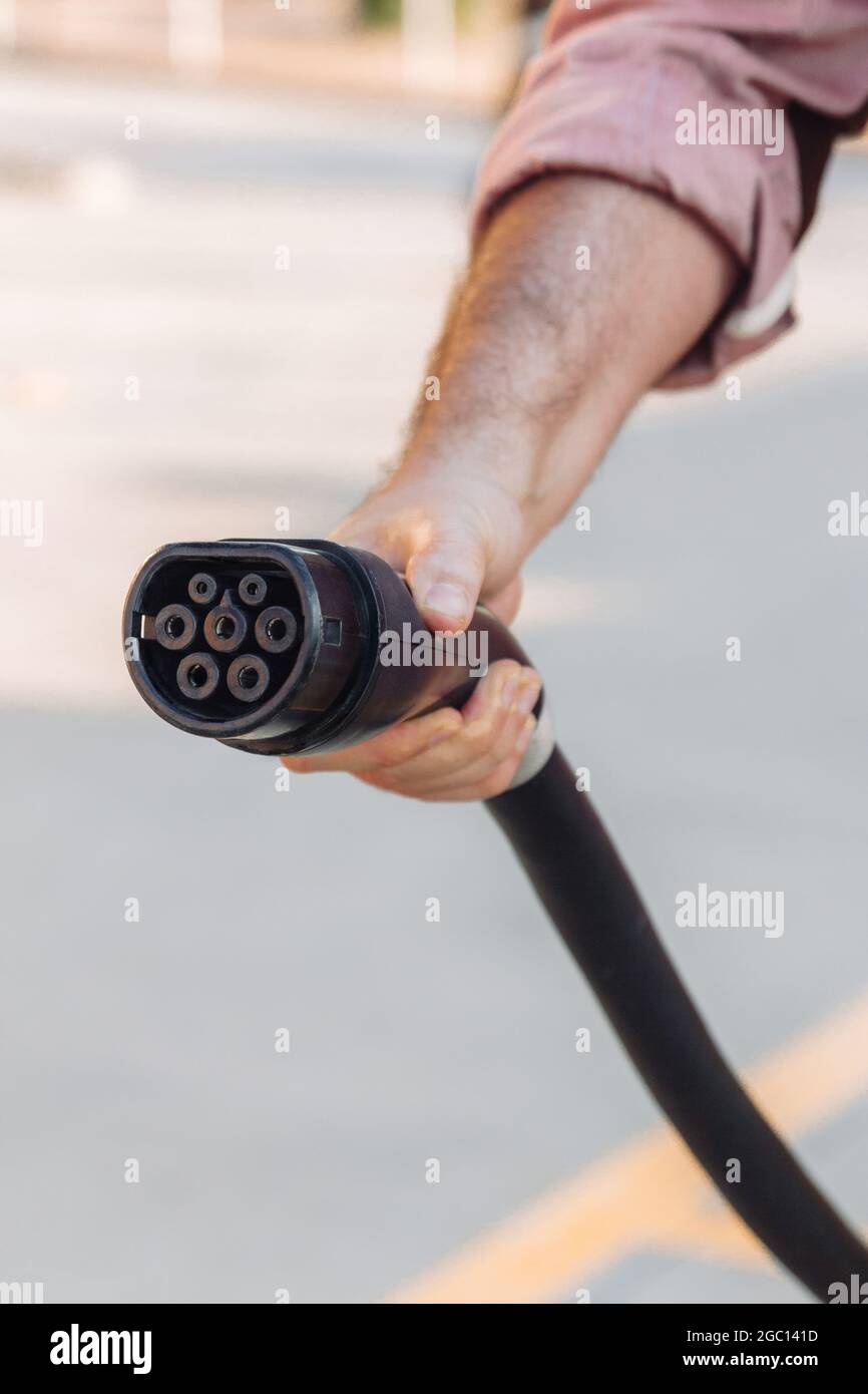 Electric vehicle or EV car socket held by a hand in a charging station. Electrical power supply and Eco-friendly alternative energy concept Stock Photo