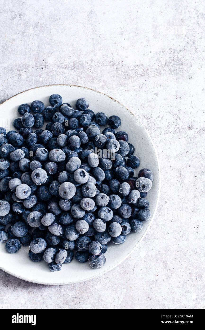 White plate with a pile of frozen blueberries on a textured background. Stock Photo