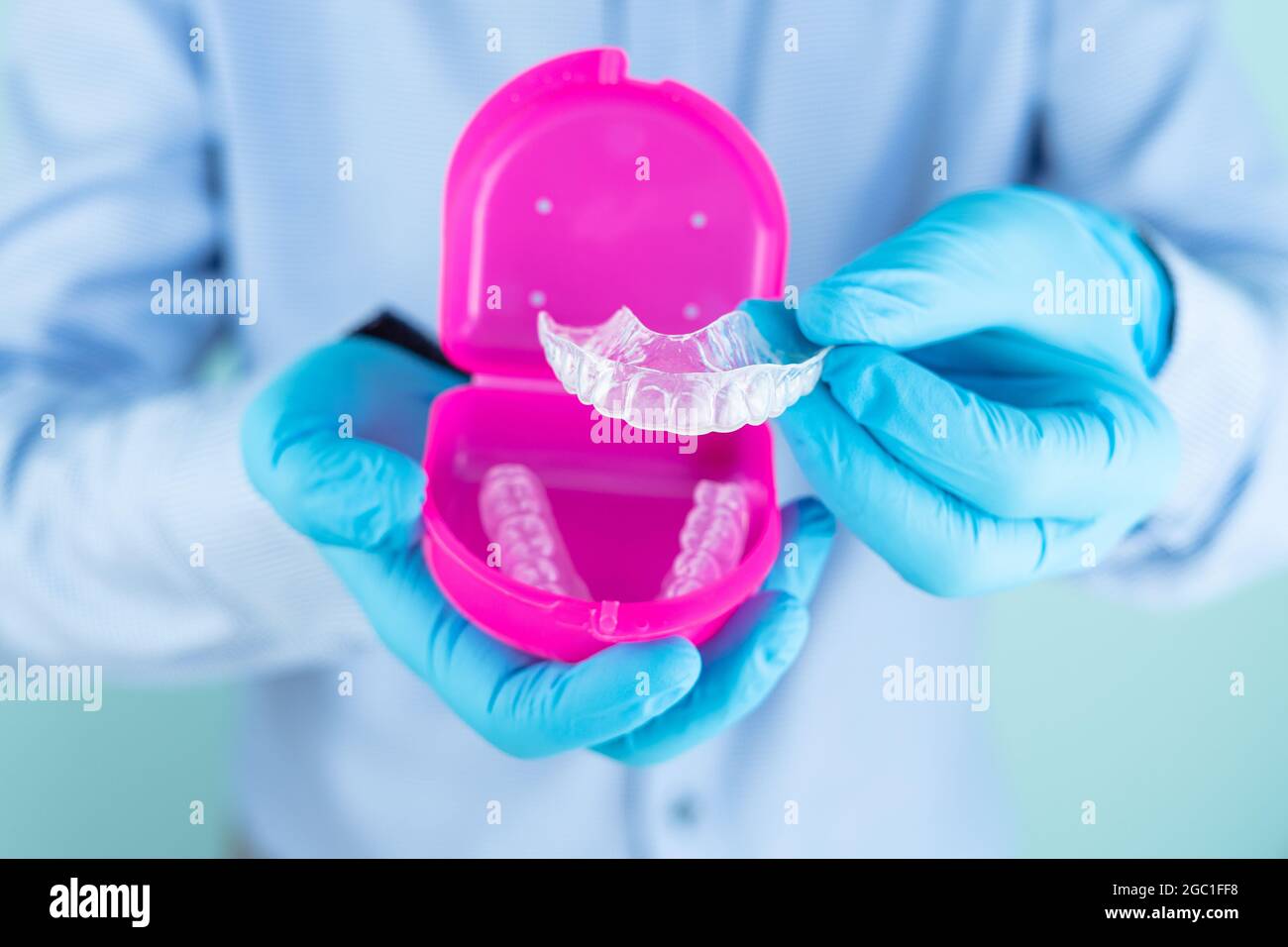 Doctor in blue shirt and gloves showing a dental splint in pink box ...