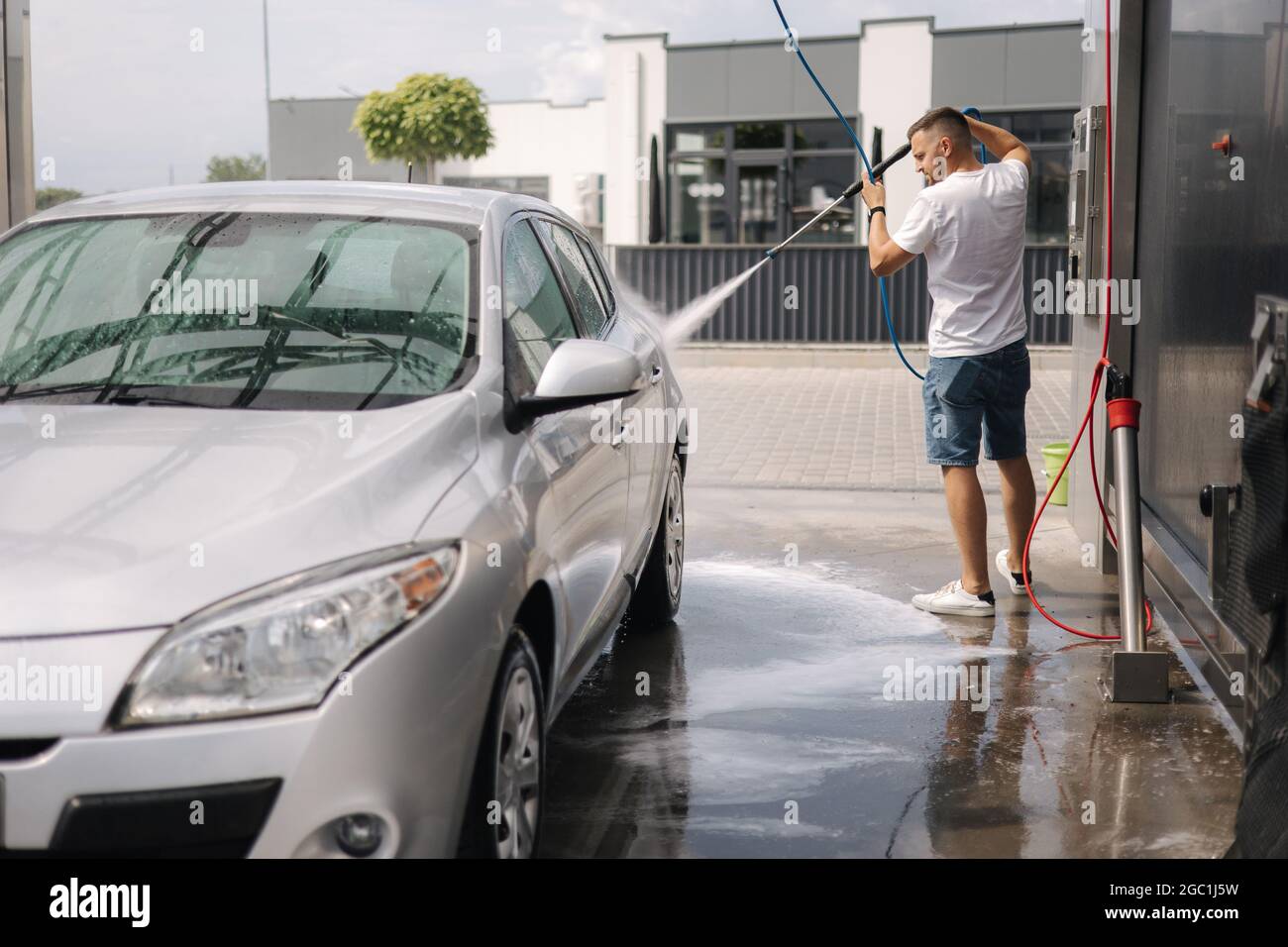 Young man cleaning his car with a jet sprayer. Selfservice car washing