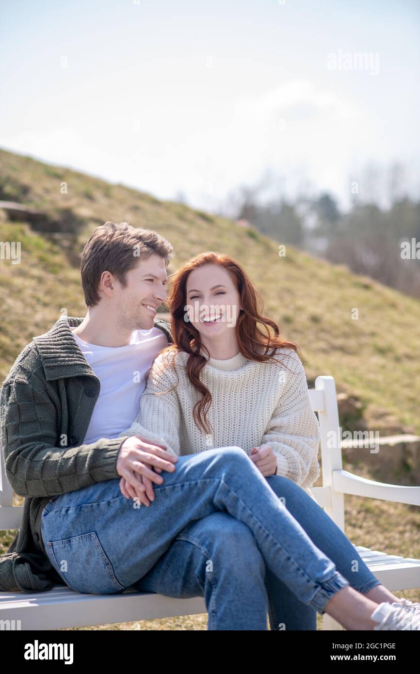 Smiling man and woman sitting on bench in nature Stock Photo
